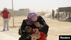 A Syrian refugee woman carries her baby as they walk amidst dust at the Al Zaatri refugee camp in the Jordanian city of Mafraq, near the border with Syria, August 13, 2012.