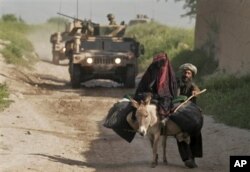 An Afghan couple with their donkey pass in front of a NATO patrol in Balamorghab district of Badghis Province, west of Kabul, Afghanistan, 12 Apr 2010
