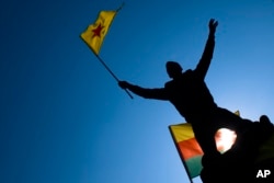FILE - A man waves a flag with Kurdish symbols as he attends a demonstration of about 1,000 protesters against the Turkish offensive targeting Kurds in Afrin, northern Syria, in Berlin, March 3, 2018.