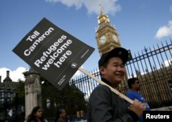 FILE - A protester holds up a placard during a demonstration in London to express solidarity with migrants and to demand the government welcome refugees into Britain, Sept. 12, 2015.