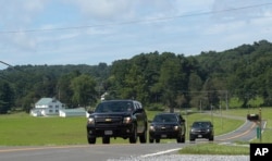 FILE - Official vehicles drive down a road near Camp David, Maryland, Aug. 18, 2017.