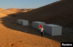 A man holds a Palestinian flag as he walks near shacks installed by activists to protest the Israeli plan to demolish the Bedouin village of Khan al-Ahmar, in Khan al-Ahmar, occupied West Bank, Sept. 11, 2018.