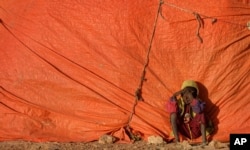 A young Somali boy sits outside his makeshift hut at a camp for people displaced from their homes elsewhere in the country by the drought, shortly after dawn in Qardho, Somalia, March 9, 2017.