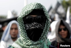 An Islamic group member covers his face with Hizbut Tahrir flag during a protest against the decree allowing the government to disband organizations deemed to run counter to the secular state, in Jakarta, Indonesia, July 28, 2017.