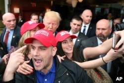 Supporter Pat Montelli shouts as he points to his hat, while friend Catherine Freeman takes a photograph with Republican presidential candidate, Donald Trump at a campaign rally in Staten Island, N.Y., April 17, 2016.