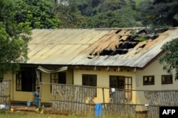 FILE - A woman stands outside the damaged roof of a school's dormitory after it was started on fire overnight in Bafut, in the northwest English-speaking region of Cameroon, Nov. 15, 2017.