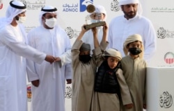 Victorious camel breeders accept a trophy for their camel at Al Dhafra Festival in Liwa desert area 120 kilometres (75 miles) southwest of Abu Dhabi, United Arab Emirates, Dec. 22, 2021.