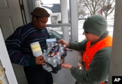 FILE - Louis Singleton receives water filters, bottled water and a test kit from Michigan National Guard Specialist Joe Weaver as clean water supplies are distributed to residents in Flint, Michigan, Jan. 21, 2016.