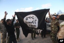 Iraqi security forces and allied Shi'ite militiamen celebrate as they hold a flag of the Islamic State group they captured in Tikrit, 80 miles (130 kilometers) north of Baghdad, March 31, 2015.