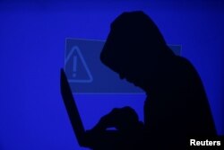 FILE - A hooded man holds a laptop computer as blue screen with an exclamation mark is projected on him in this illustration picture taken on May 13, 2017.