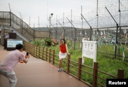 A woman poses for photographs in front of a barbed-wire fence near the demilitarized zone separating the two Koreas in Paju, South Korea, July 14, 2017.