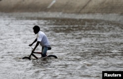 FILE - A boy rides a bicycle in floodwater in the old quarter of Sana'a, Yemen, August 9, 2017.