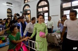 Myanmar's opposition leader Aung San Suu Kyi, center, greets a patient in a bed at Yangon General Hospital in Yangon, Myanmar, Oct. 30, 2015.