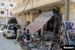 FILE - Residents work on fixing a damaged shop in the town of Darat Izza, province of Aleppo, Syria, Feb. 28, 2016.