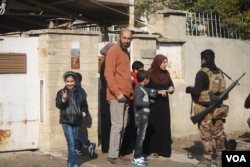 Six-year-old Aya, left, flashes a victory sign as her family speaks to Iraqi soldiers, sharing information about local IS militants that had been defeated in Mosul, Iraq, two days prior to Jan. 23, 2017. (H. Murdock/VOA)