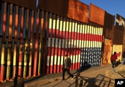 FILE - People pass graffiti along the border structure in Tijuana, Mexico, Jan. 25, 2017.