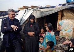 FILE - Filippo Grandi, left, the U.N. High Commissioner for Refugees, speaks with a Syrian family at a camp in Saadnayel, in the Bekaa valley, Lebanon, Jan. 22, 2016. Grandi said nearly two-thirds of refugees are women and children.