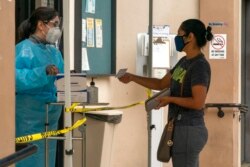 FILE - A patient shows her COVID-19 vaccination card at the Clínica Monseñor Oscar A. Romero in the Pico-Union district of Los Angeles, July 26, 2021.