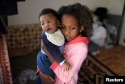 A displaced Libyan girl, who fled her house because of the fighting between the Eastern forces commanded by Khalifa Haftar and the internationally recognized government, carries her son at the industrial complex, which is used as a shelter, in Tripoli, Li