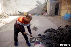 FILE - A man shovels coal he uses to heat his home in his courtyard in the village of Heqiaoxiang outside of Baoding, Hebei province, China, Dec. 5, 2017.