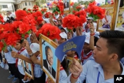 Cambodian students hold flowers and portraits of their king, Norodom Sihamoni, upper right, and former king, Norodom Sihanouk, center, during Independence Day celebrations in Phnom Penh, Cambodia, Nov. 9, 2017.