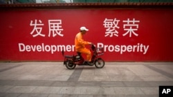 FILE - A maintenance worker rides a scooter past banners reading "Development" and "Prosperity" in English and Chinese on a street in central Beijing, July 15, 2015. An estimated $1 trillion dollars are needed to underpin Asia's growth.
