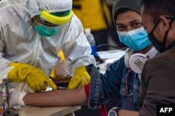 Para petugas kesehatan melakukan pemeriksaan kesehatan 156 pekerja migran Indonesia yang tiba dari Malaysia di Bandara Juanda, Surabaya, 7 April 2020. (Foto: AFP)