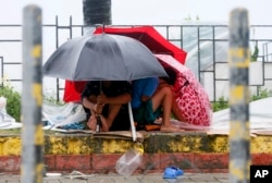 Residents huddle together under their umbrellas as strong winds and slight rain are brought by Typhoon Koppu, Oct. 18, 2015 in Manila, Philippines.