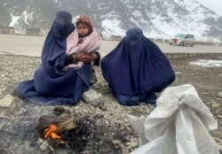 Gulnaz (kiri), dan putranya yang berusia 18 bulan menghangatkan diri saat mereka menunggu sedekah di jalan raya Kabul - Pul-e-Alam Afghanistan timur, Selasa, 18 Januari 2022.
