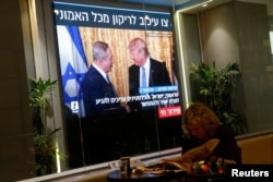 FILE - A woman reads a newspaper as monitors showing the meeting between U.S. President Donald Trump and Israeli Prime Minister Benjamin Netanyahu in Washington are seen next to a coffee shop in Tel Aviv, Israel, Feb. 15, 2017.
