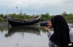 FILE - An Acehnese woman uses her mobile phone to take pictures of the boat carrying a group of ethnic-Rohingya that was brought ashore in Bireuen, Aceh province, Indonesia, April 20, 2018.
