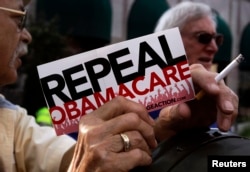 FILE - Demonstrators stand outside a hotel before former South Carolina Senator Jim DeMint, president of The Heritage Foundation, speaks at a "Defund Obamacare Tour" rally in Indianapolis, Aug. 26, 2013.