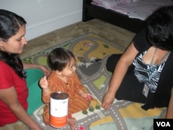 With Vijan's mother Bhawana looking on, family support worker Tina Fontaine uses play time to help develop the baby's motor skills. (VOA/J. Taboh)