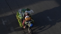 ស្ត្រីម្នាក់កំពុងធ្វើដំណើរតាមម៉ូតូដឹកផ្លែឈើនិងបន្លែនៅលើដងវិថីមួយ ក្នុងរាជធានីភ្នំពេញ ថ្ងៃទី១៧ ខែសីហា ឆ្នាំ២០២០។