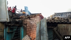 Des gens sur un toit tentant de combattre un incendie qui s'est déclaré sur le marché de Bouaké, dans le centre de la Côte d'Ivoire, le 27 août 2019. (Photo by STR / AFP)