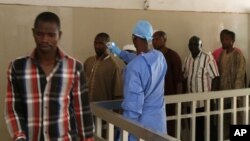 FILE - A health worker, center, takes the temperature of people to see if they might be infected by the Ebola virus inside the Ignace Deen government hospital in Conakry, Guinea, March 18, 2016.