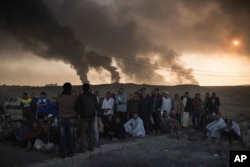 Men are held by Iraqi national security agents, to be interrogated at a checkpoint, as oil fields burn in Qayyarah, south of Mosul, Iraq, Nov. 5, 2016.