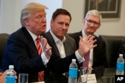 Apple CEO Tim Cook, right, and PayPal founder Peter Thiel, center, listen as President-elect Donald Trump speaks during a meeting with technology industry leaders at Trump Tower in New York, Dec. 14, 2016.
