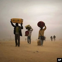 Men, who used to work in Libya and fled the unrest in the country, carry their belongings as they walk during a sand storm in a refugee camp at the Tunisia-Libyan border, in Ras Ajdir, Tunisia, March 15, 2011