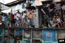 FILE - An agent of the Philippine Drug Enforcement Agency, at right, escorts suspects during a raid at an informal settlers' area inside a public cemetery in Manila, March 16, 2017.