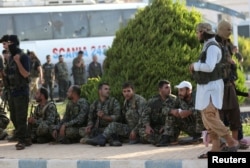 Islamist rebels from Hayat Tahrir al-Sham stand near a group of fighters loyal to President Bashar al Assad from the villages of al-Foua and Kefraya, Syria, July 19, 2018.