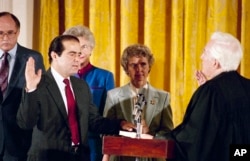 Retiring Chief Justice Warren Burger, right, administers an oath to Antonin Scalia, as Scalia's wife Maureen holds the bible in the East Room of White House, Sept. 26, 1986.