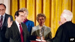 Retiring Chief Justice Warren Burger, right, administers an oath to Antonin Scalia, as Scalia's wife Maureen holds the bible in the East Room of White House, Sept. 26, 1986.