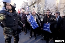 An Iranian riot policeman stands guard as protesters hold street signs with the name of Shi'ite cleric Sheikh Nimr al-Nimr during a demonstration condemning his execution in Saudi Arabia, outside the Saudi Arabian Embassy, in Tehran, Jan., 3, 2016.