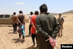 FILE - Men, who the Democratic Forces of Syria fighters claimed were Islamic State fighters, walk as they are taken prisoners after SDF advanced in the southern rural area of Manbij, in Aleppo Governorate, Syria, May 31, 2016.
