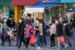 FILE - In this March 30, 2021, file photo, people cross a busy street in the shopping district of Flushing, a largely Asian American neighborhood in the Queens borough of New York. (AP Photo/Kathy Willens, File)