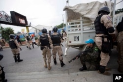 FILE - A U.N. peacekeeper takes cover behind national police officers while demonstrators throw rocks, during a protest against the country's electoral council to mark the 25th anniversary of first democratic election in 1990, in Port-au-Prince, Haiti.