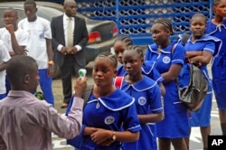 FILE – A Liberian teacher takes the temperature of arriving students as part of Ebola prevention measures at BW Harris High School in Monrovia, Feb. 16, 2015.