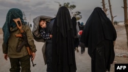 Veiled women, reportedly wives and members of the Islamic State, walk under the supervision of a female fighter from the Syrian Democratic Forces (SDF) at al-Hol camp in al-Hasakeh governorate in northeastern Syria, Feb. 17, 2019.