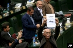 Iranian conservative lawmaker Bijan Nobaveh Vatan holds up a paper with writing in Persian reading, "Opponent of the JCPOA," in an open session of parliament while discussing a bill on the deal, in Tehran, Iran, Oct. 11, 2015.